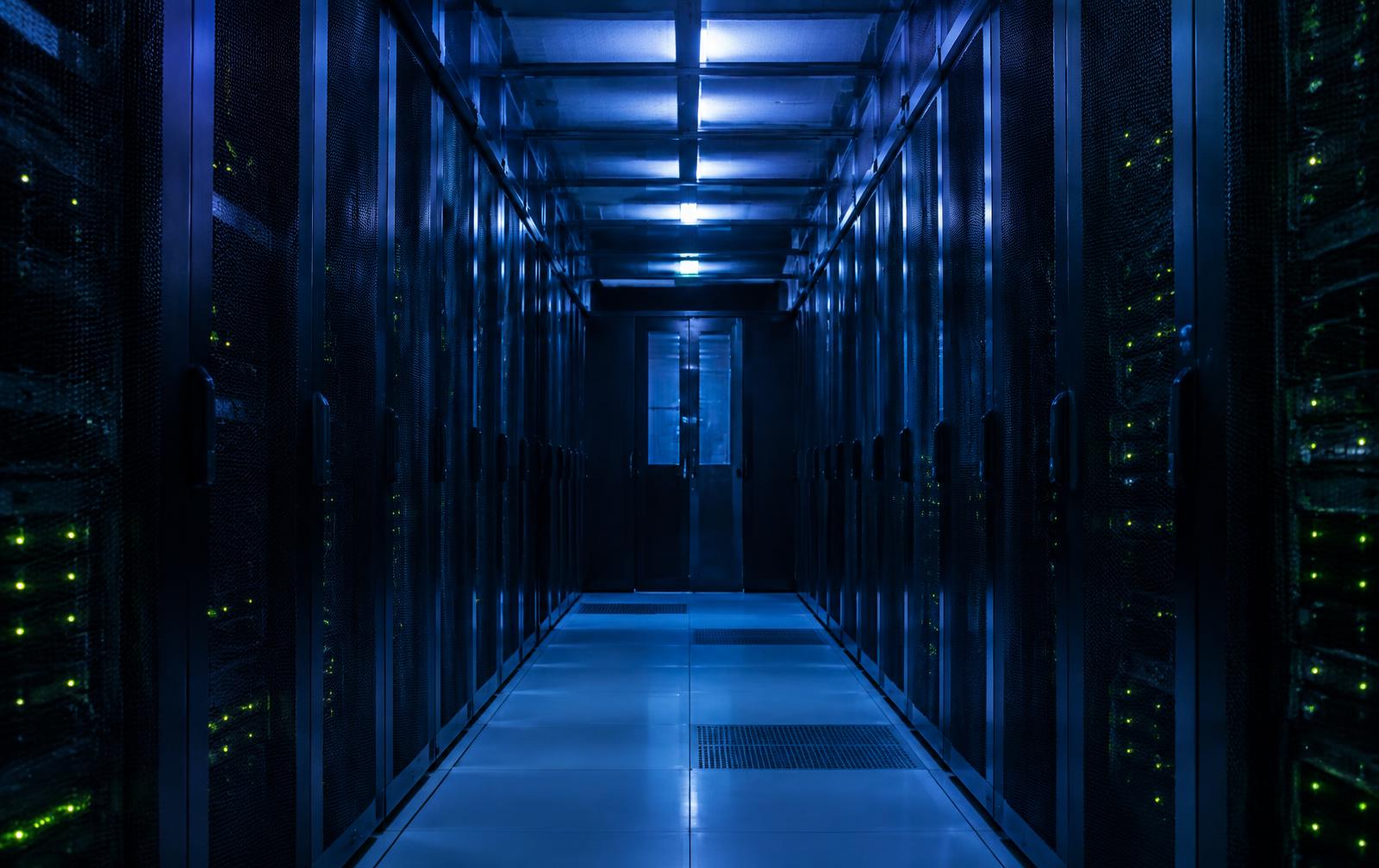 Corridor of server racks in a data centre lit in cool blue tones